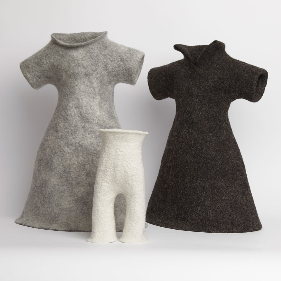 Das Bild zeigt drei aus Wolle gefilzte Skulpturen in Hellgrau, Dunkelgrau und Weiß. Die grauen Skulpturen stellen Kleider dar, das Weiße ist eine Hose.